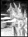 Greyscale dragon perched on rooftop of gothic house.